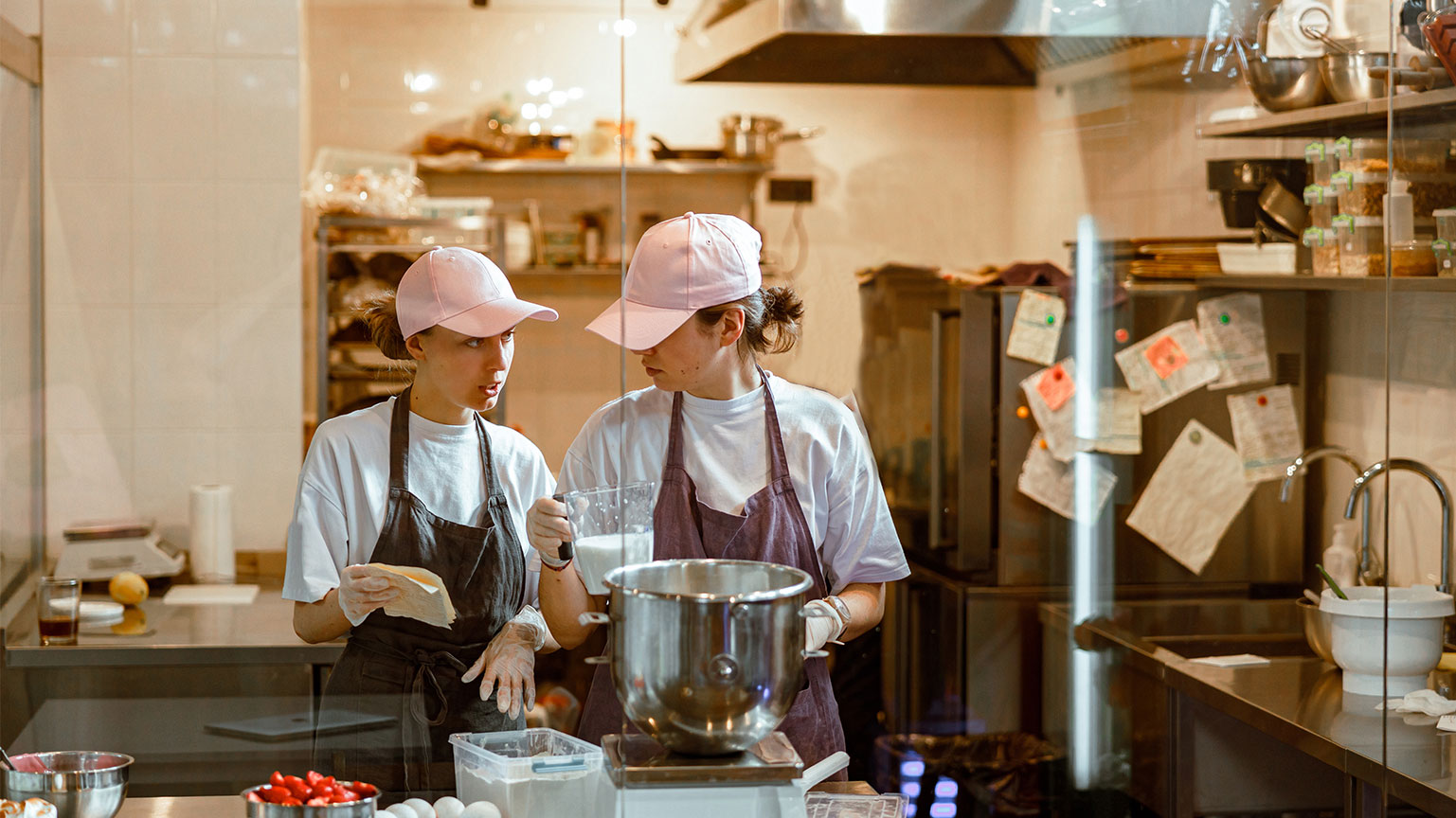 woman-shows-recipe-to-colleague-making-dough-at-ta-2025-03-26-12-15-23-utc